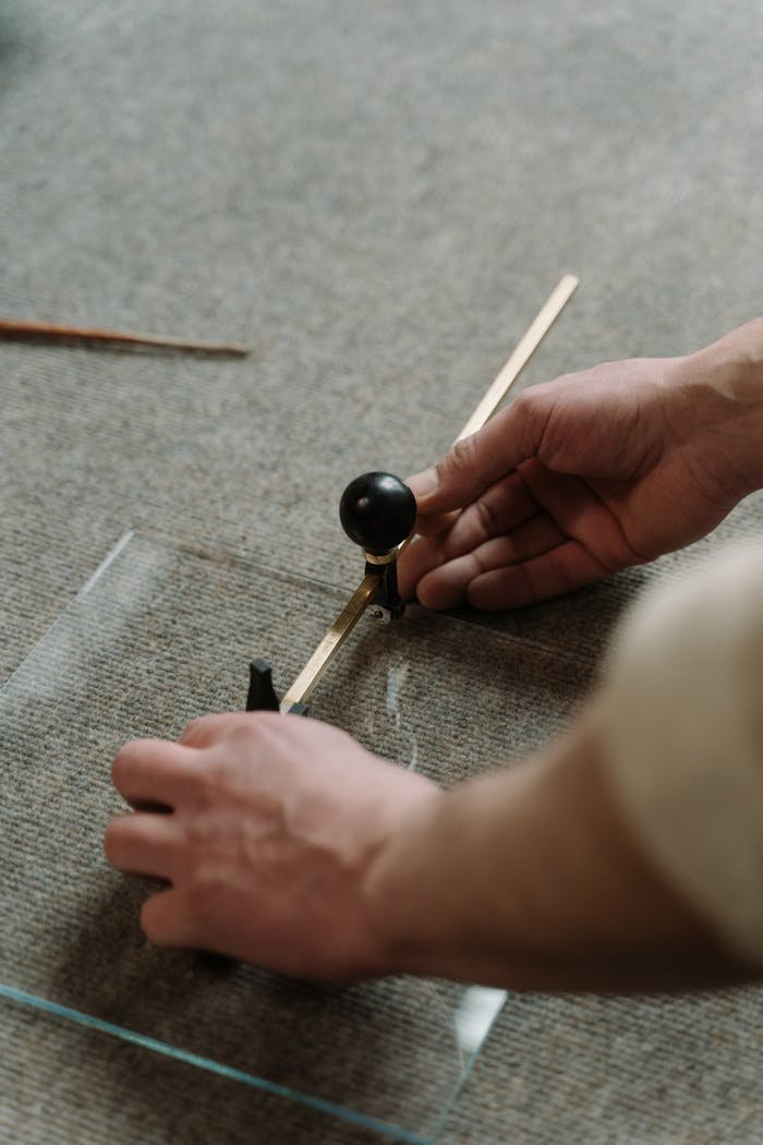 Hands of a craftsman carefully cutting glass with a tool, showcasing precision and skill.